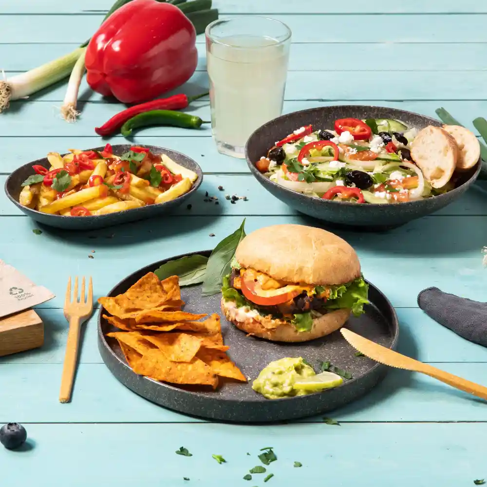 Un burger avec de la laitue, de la tomate et de la sauce, servi avec des chips tortilla et du guacamole, accompagné d'une salade et de frites.