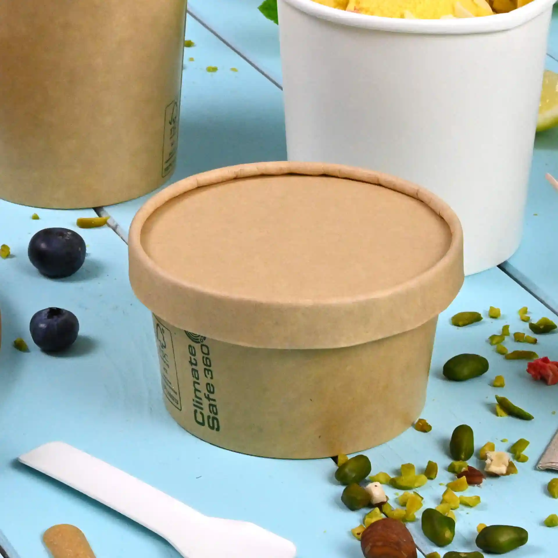 Conteneur rond en carton brun avec un couvercle, placé sur une surface bleue, entouré d'aliments et d'une cuillère en plastique.