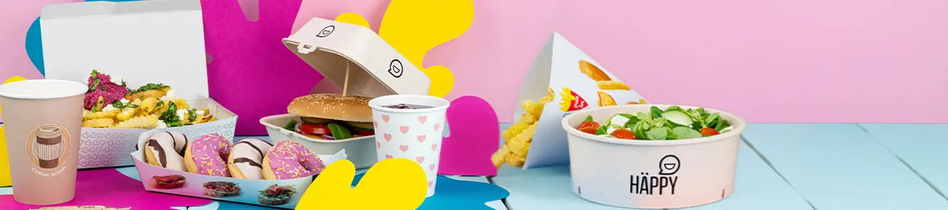 Arrangement de fast-food à emporter avec un burger, frites, bol de salade coloré, sauce et boisson sur une surface bleue.